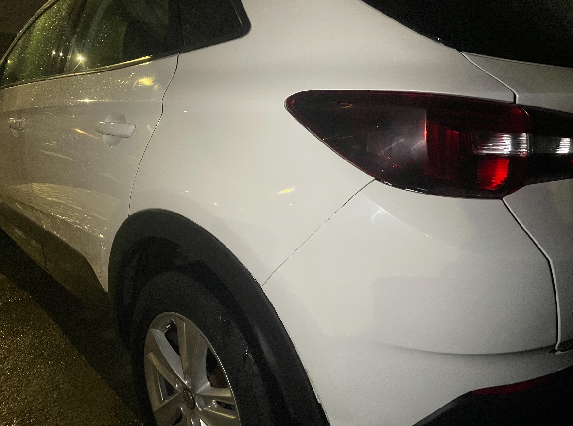 A white SUV's rear wing and bumper after its repair, photographed in the evening